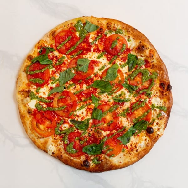 MONDO PIZZA's Margherita pizza with fresh tomatoes, basil, and pesto drizzle on a white surface.