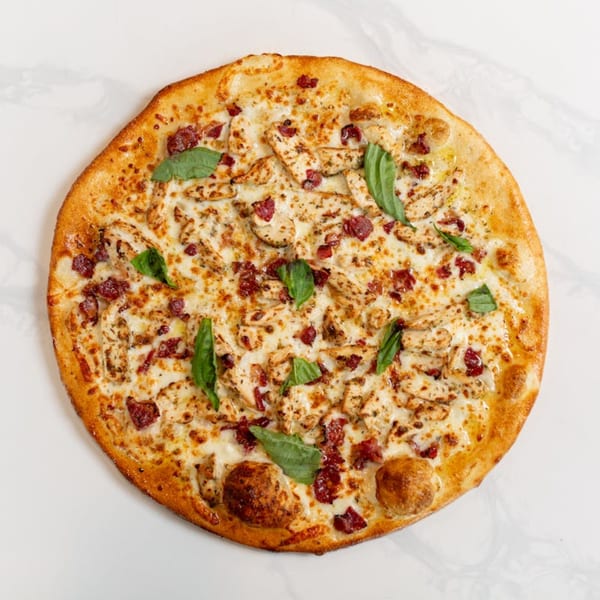 MONDO PIZZA's chicken and bacon pizza, topped with fresh basil, on a white marble surface.
