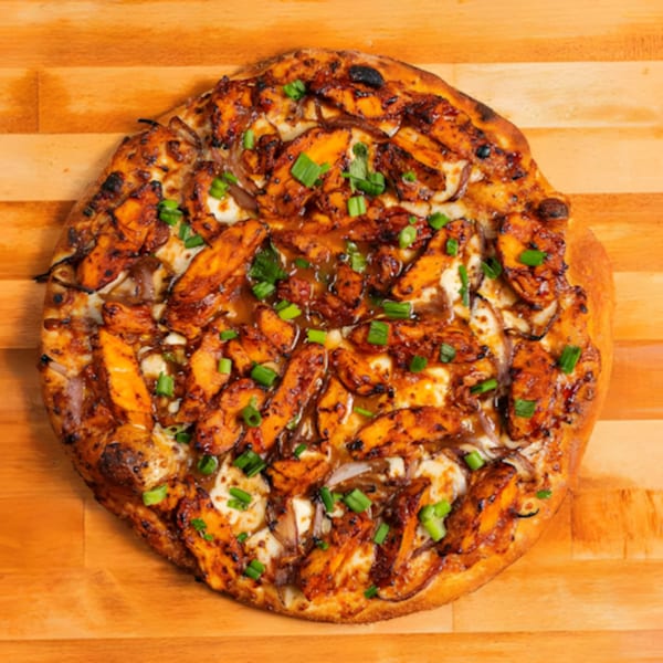MONDO PIZZA's BBQ chicken pizza with onions and green onions on a wooden surface.