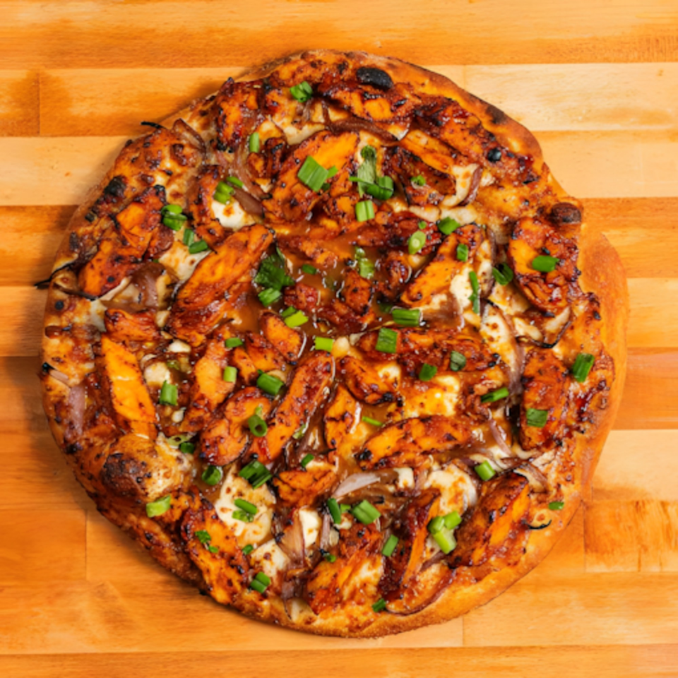 MONDO PIZZA's BBQ chicken pizza with onions and green onions on a wooden surface.