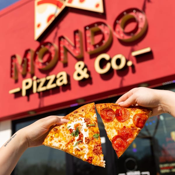 Two hands holding slices of pepperoni and corn pizza in front of the MONDO Pizza & Co. sign.