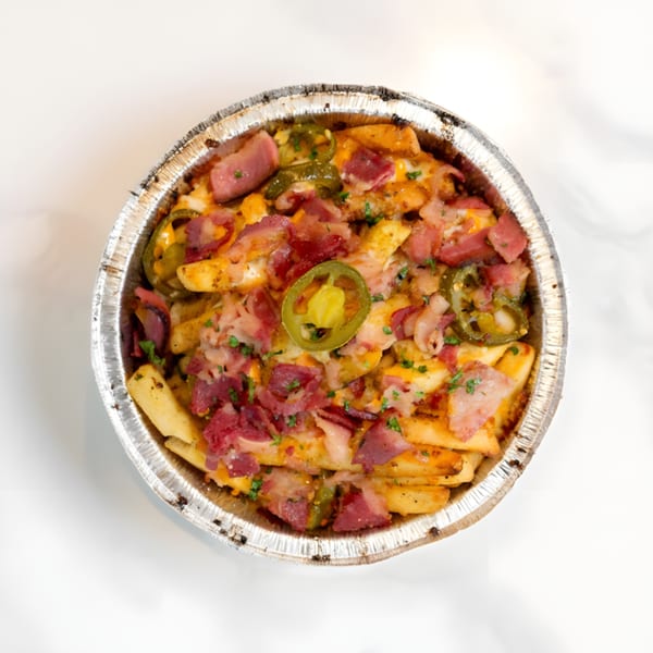 Loaded fries in a foil pan, topped with cheese, bacon, and sliced jalapeños.