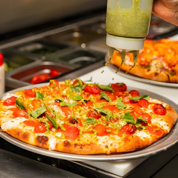 MONDO PIZZA chef drizzling pesto on a fresh pizza with cherry tomatoes and basil.