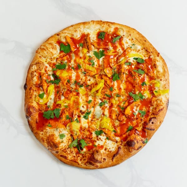 A whole MONDO PIZZA with chicken, yellow peppers, red sauce, and cilantro on a white surface.