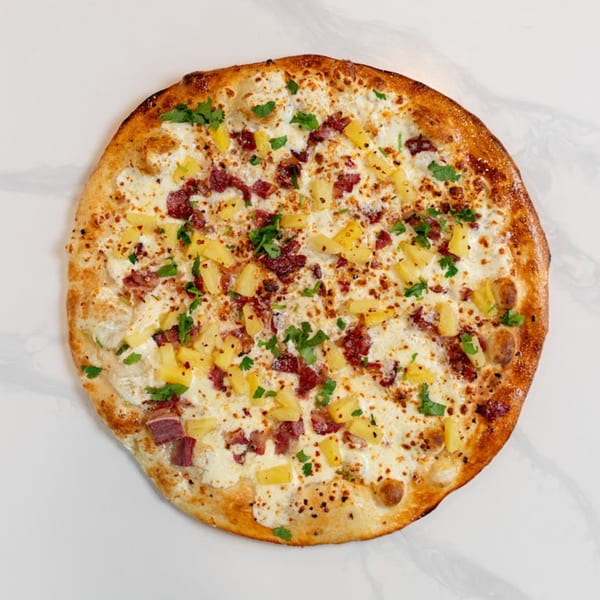 MONDO PIZZA's Hawaiian pizza with white sauce, bacon, pineapple, and parsley on a white surface.