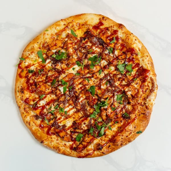 MONDO PIZZA's BBQ chicken pizza, topped with red onions, cilantro, and a drizzle of sauce.