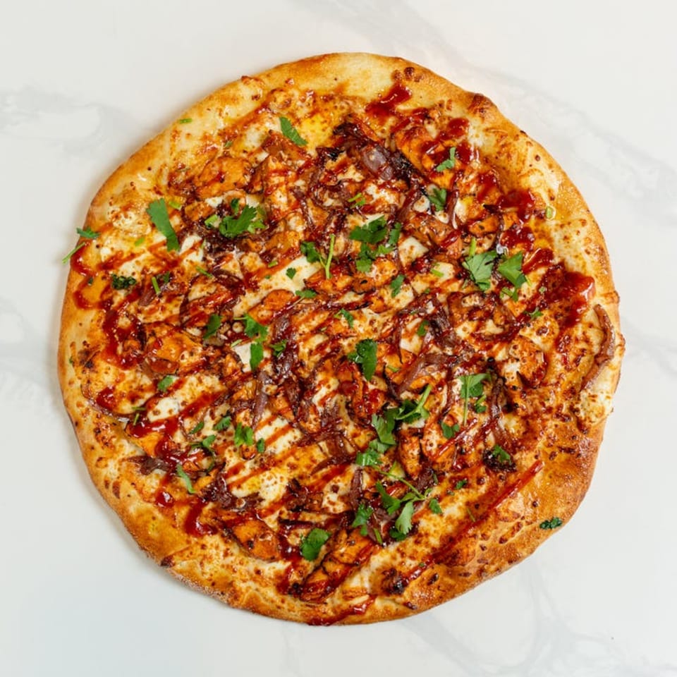 MONDO PIZZA's BBQ chicken pizza, topped with red onions, cilantro, and a drizzle of sauce.
