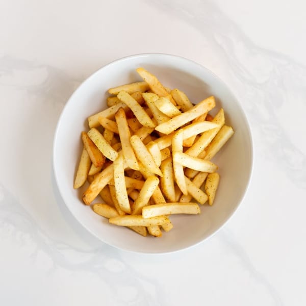 A white bowl filled with golden, seasoned french fries on a white marble surface.