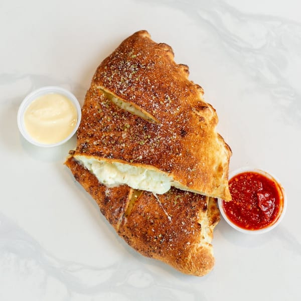 A golden-brown calzone, sliced open to reveal melted cheese, served with marinara and cheese dipping sauces.